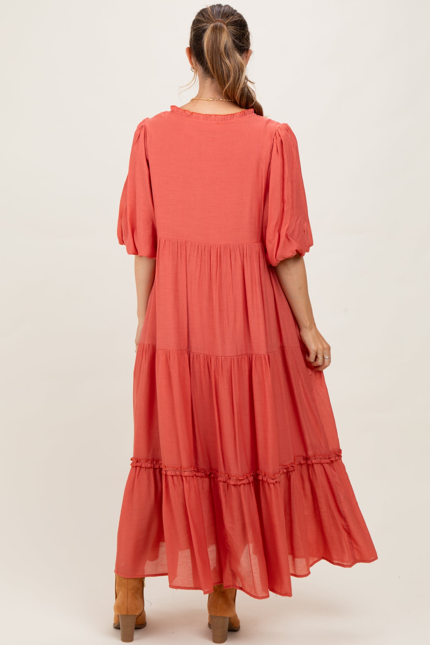 woman wearing a coral maternity maxi dress with puff sleeves and tiered ruffle details from the back
