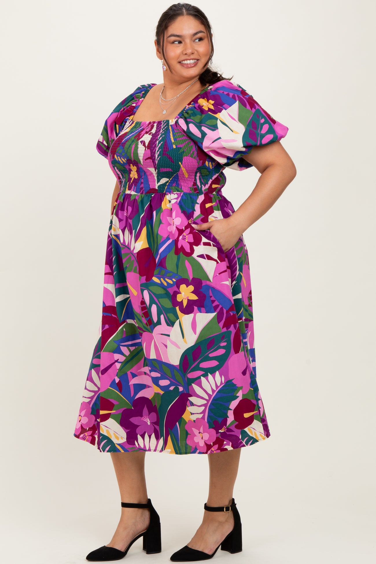 woman wearing a colorful floral plus-size dress with short puff sleeves and pockets.