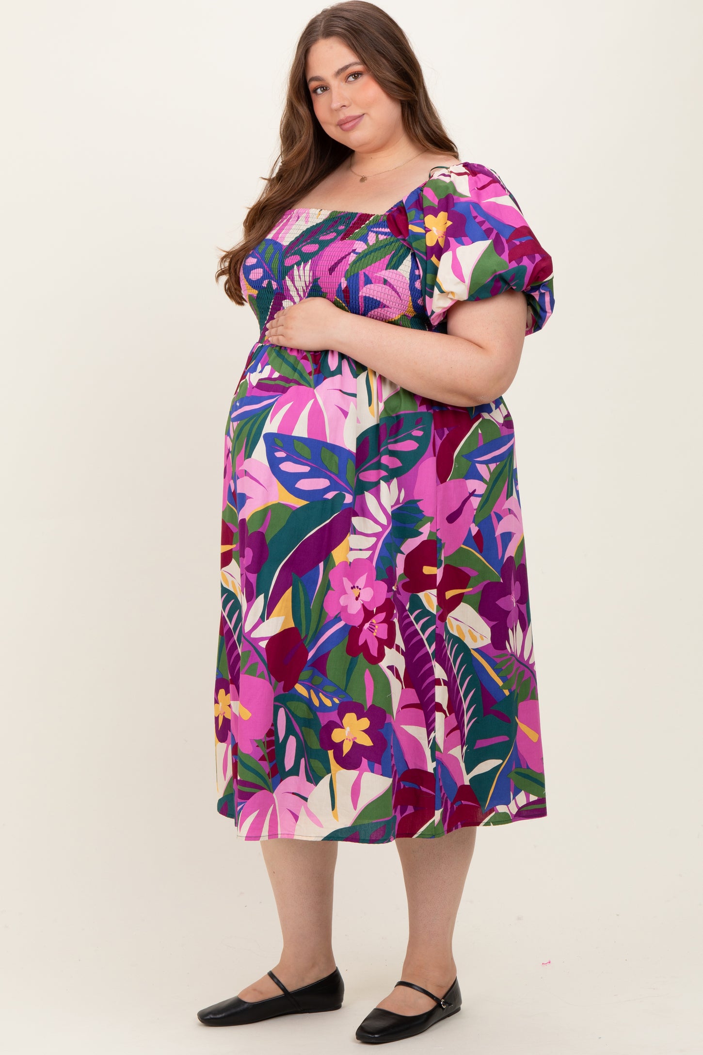 woman wearing a vibrant floral print maternity dress with puff sleeves and a hand on her baby bump