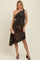 woman wearing a brown and black leopard print one-shoulder maternity dress with ruching, holding a clutch and wearing heels