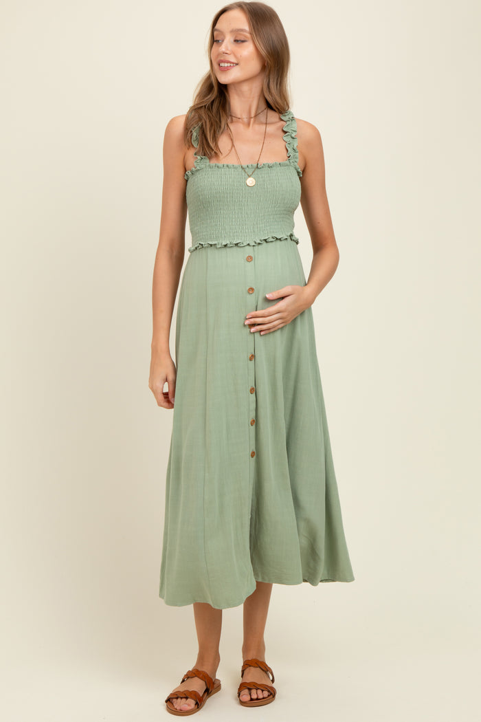 woman wearing a light green maternity dress with ruffled straps, smocked bodice, and button details, holding her baby bump