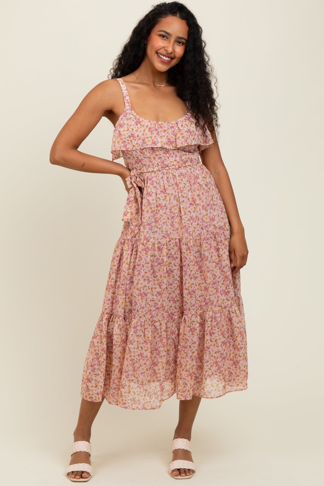 woman wearing a floral pink sundress with ruffled straps and a tiered skirt, standing and smiling