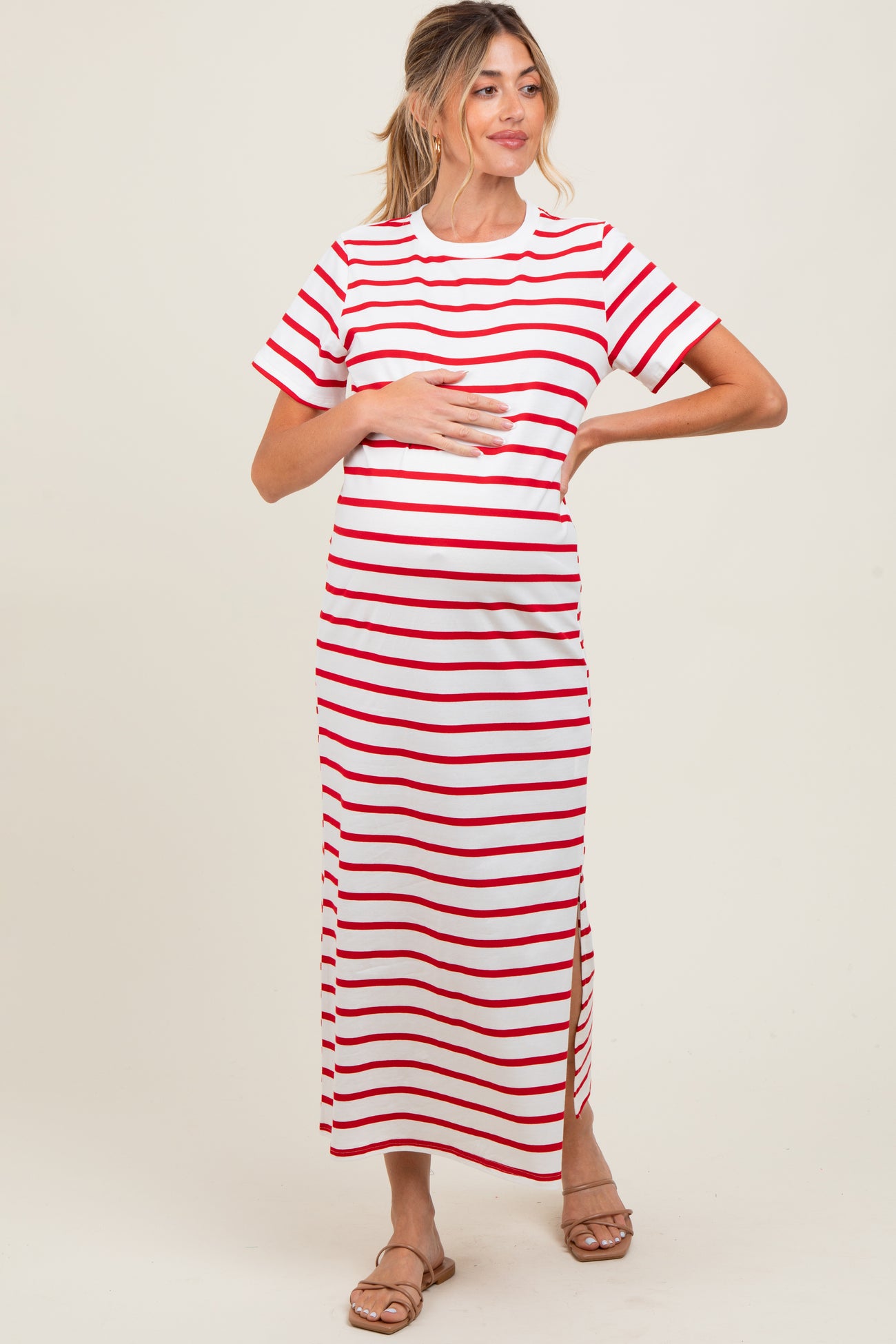 woman wearing a white and red striped maternity maxi dress with short sleeves and a side slit, holding her baby bump