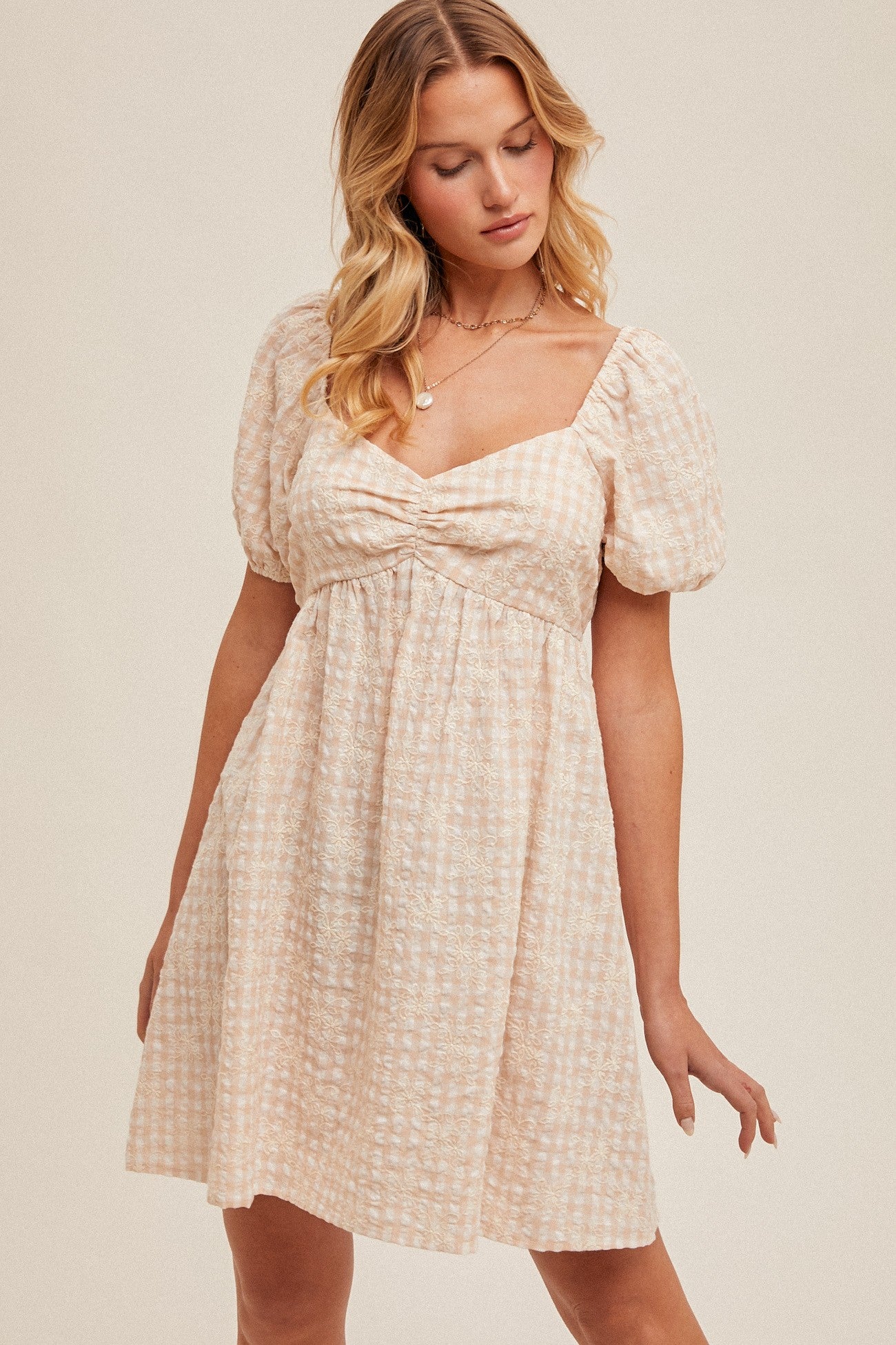 woman wearing a light pink checkered puff sleeve dress with a square neckline and a gathered waist