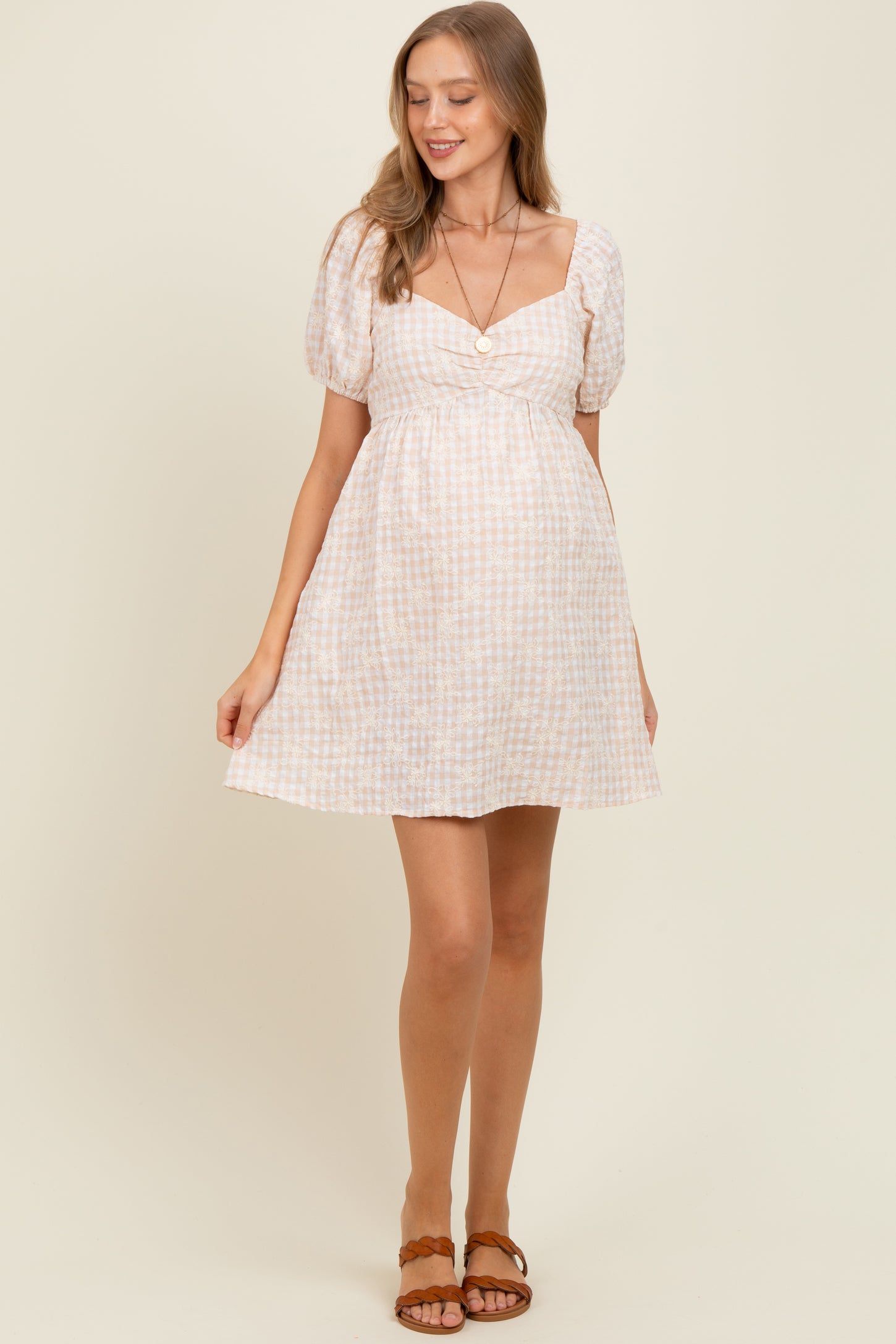 woman wearing a light pink and white checkered maternity dress with puff sleeves and a fitted bodice, showing her baby bump