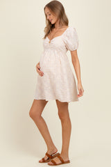 woman wearing a light pink and white checkered maternity dress with puff sleeves and a baby bump visible