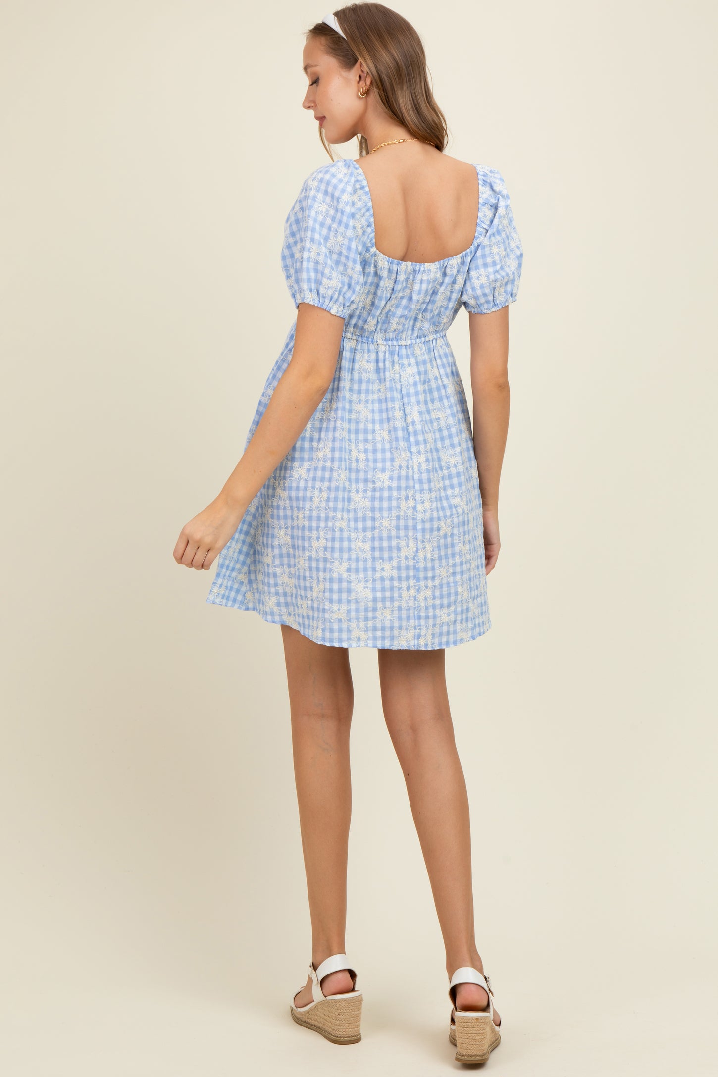 woman wearing a blue and white checkered maternity dress with puff sleeves and a cinched waist, shown from the back