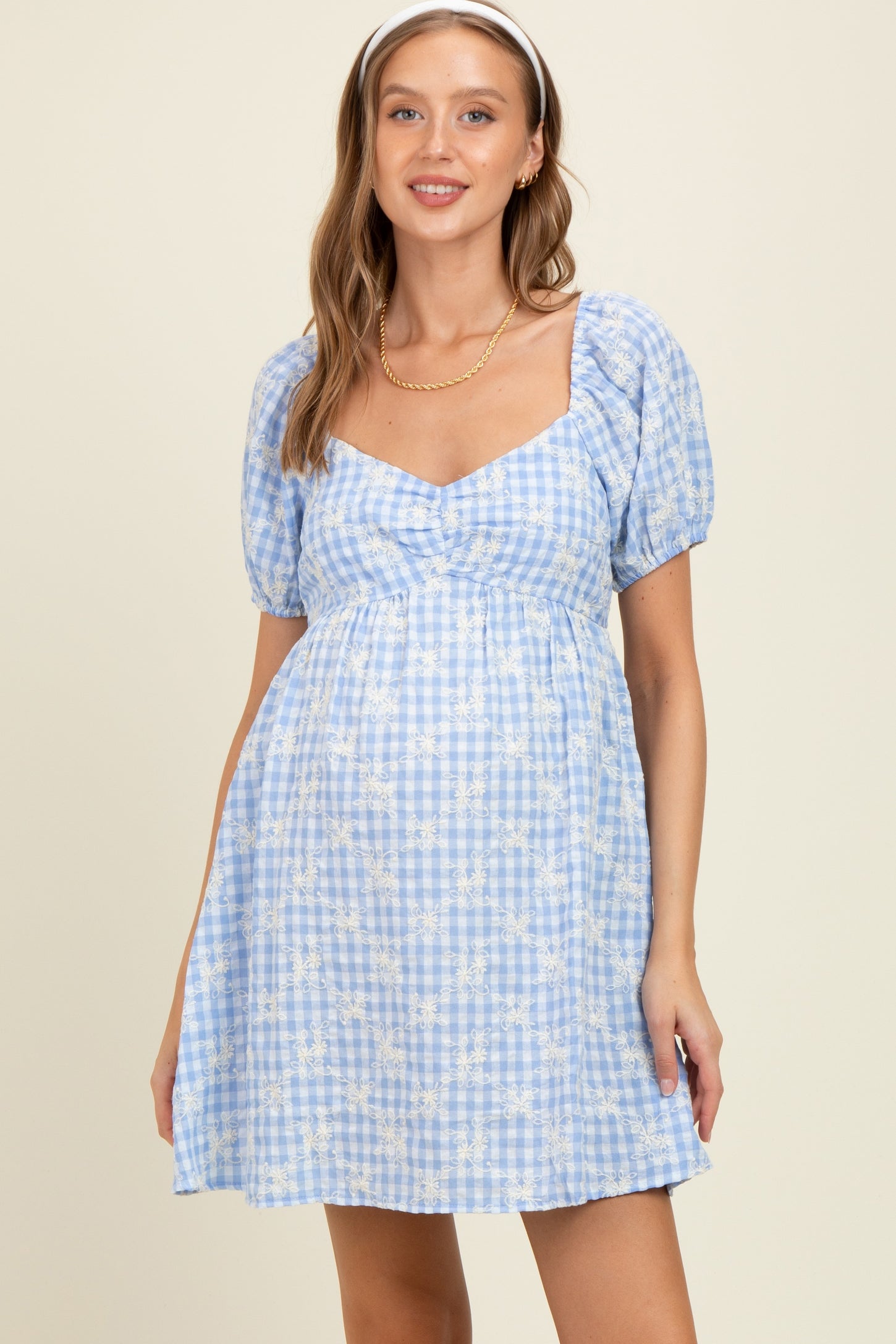 woman wearing a blue gingham maternity dress with puff sleeves and a fitted bodice, showing her baby bump