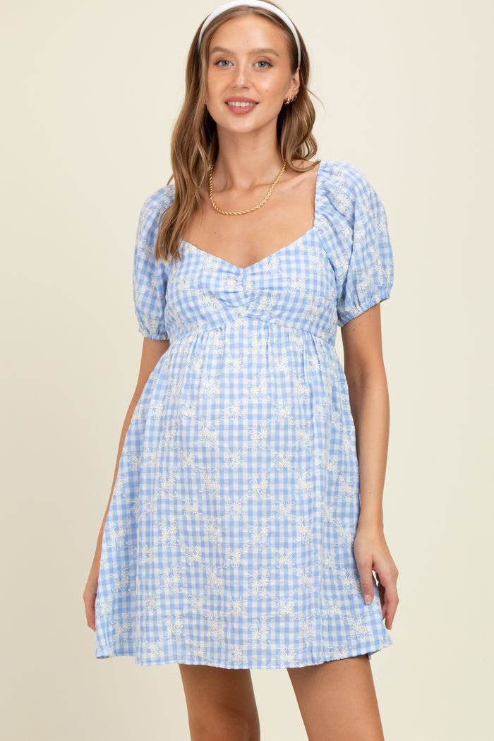 woman wearing a blue gingham maternity dress with puff sleeves and a fitted bodice, showing her baby bump