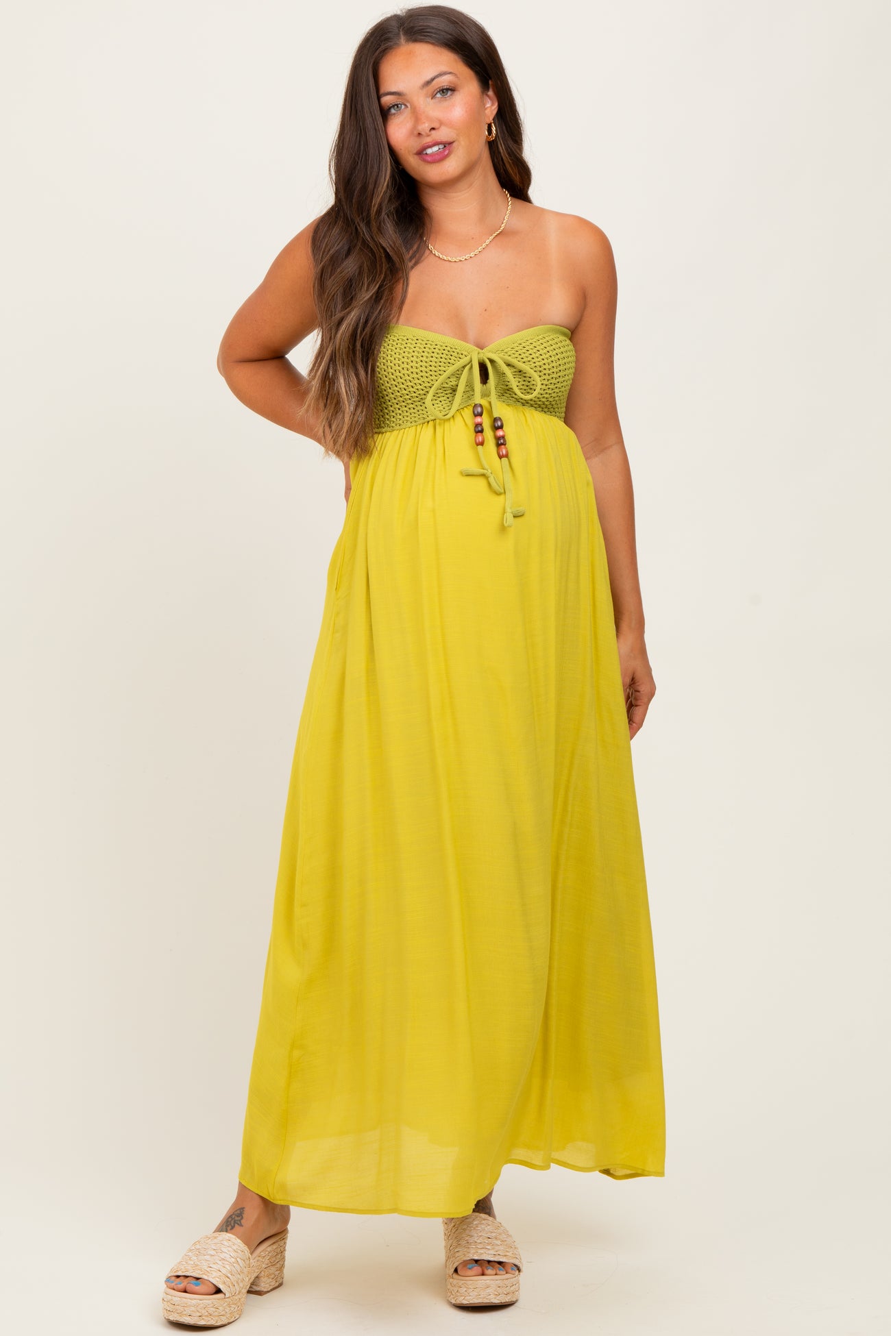 woman wearing a yellow maternity maxi dress with a crochet bodice and tie detailing, showcasing her baby bump