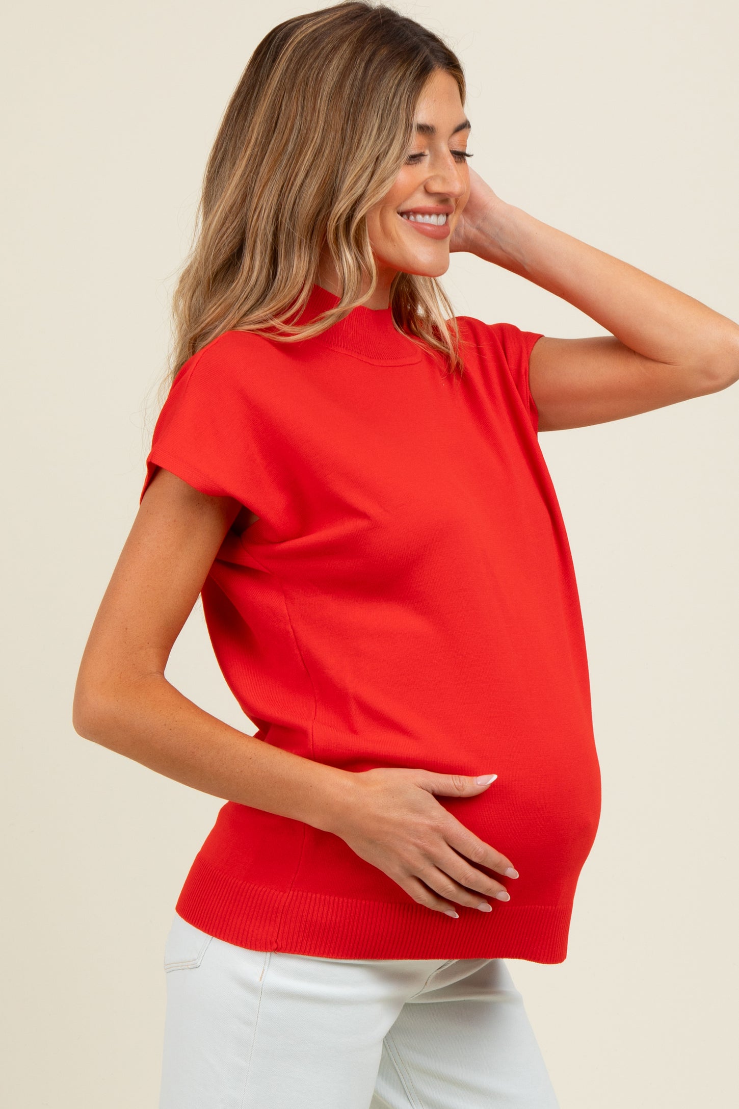 woman wearing a bright red maternity top and holding her baby bump with a smile