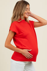woman wearing a bright red maternity top and holding her baby bump with a smile