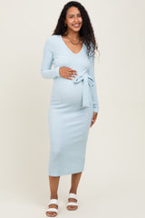woman wearing a light blue ribbed maternity dress with long sleeves and a tie waist, showing her baby bump