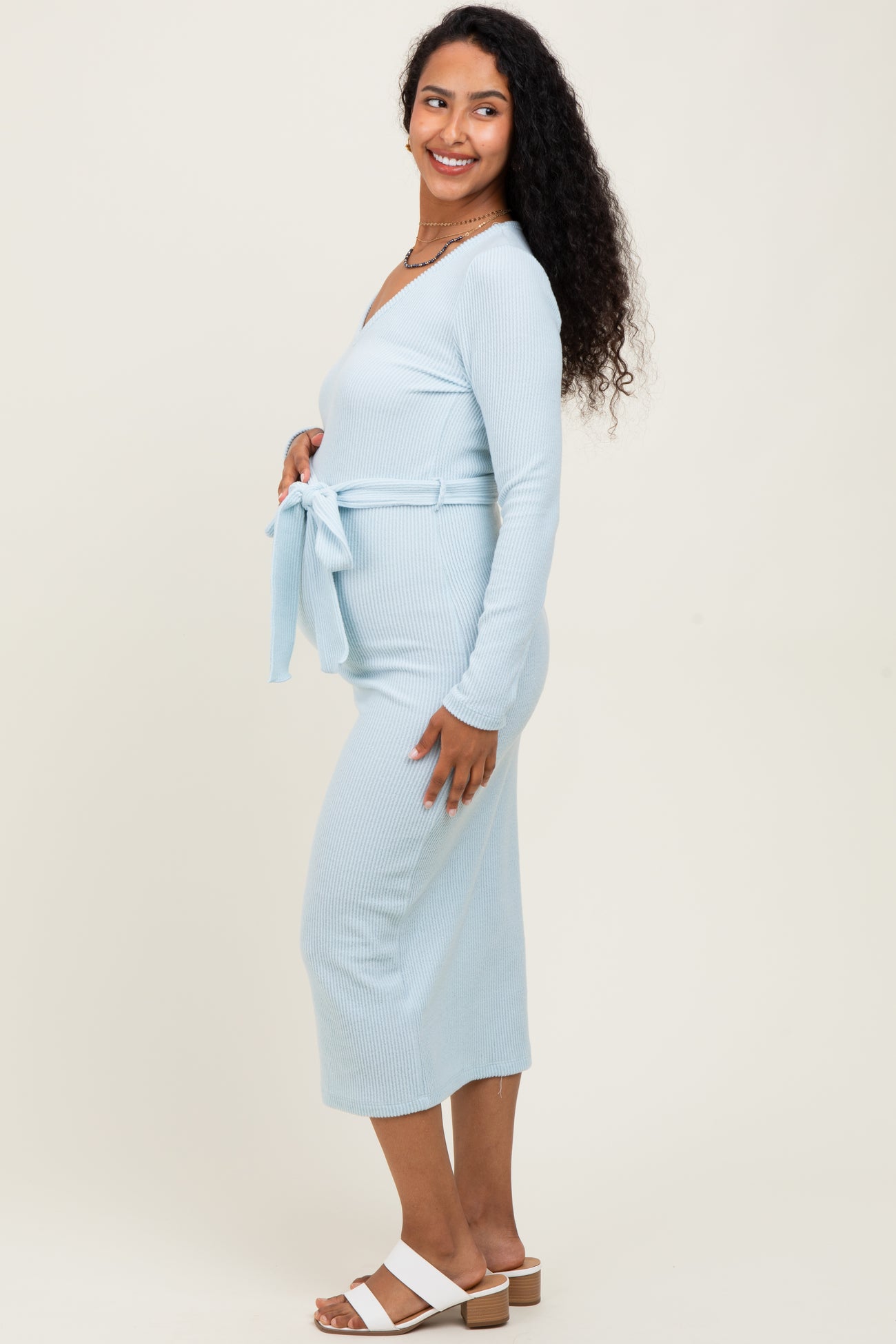 woman wearing a light blue long sleeve maternity dress with a tie at the waist and a visible baby bump