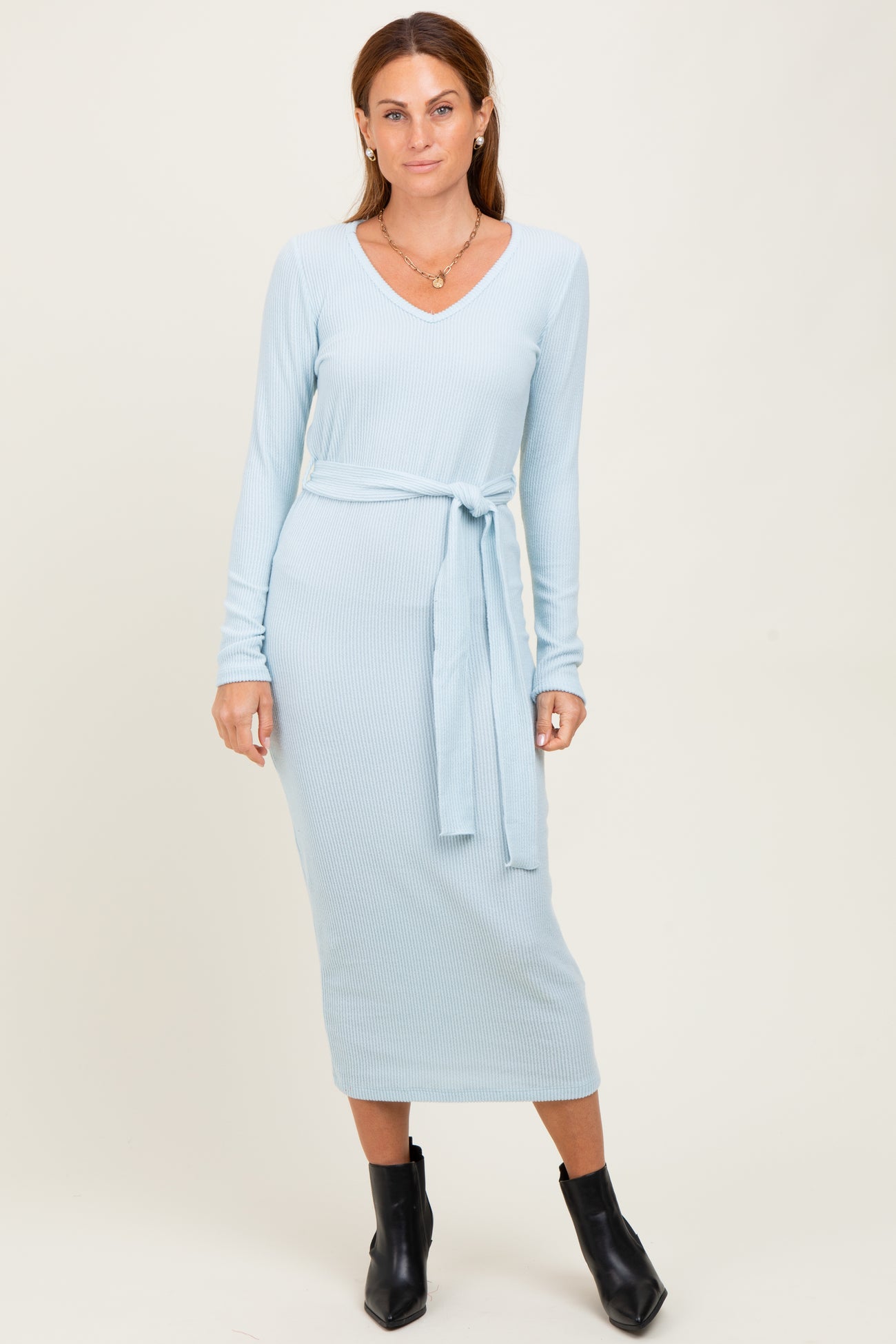 woman wearing a light blue ribbed midi dress with long sleeves and a tie belt, standing against a neutral backdrop