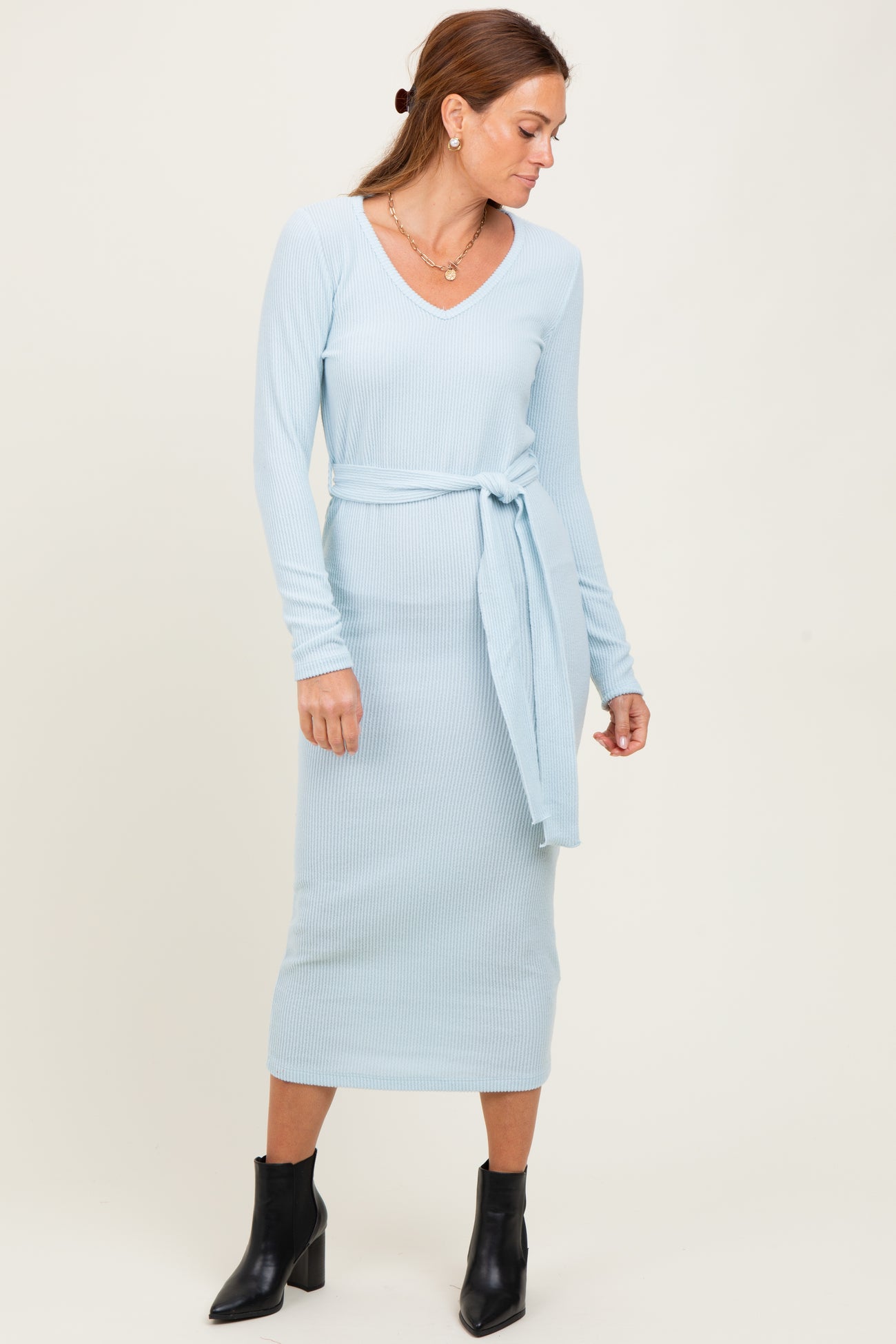 woman wearing a light blue ribbed long sleeve midi dress with a tie belt and black ankle boots