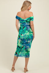 woman wearing a green and blue floral off-shoulder maternity dress with ruched detailing, showing her baby bump from the back