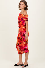 woman wearing a vibrant orange tropical print off-the-shoulder midi dress with ruching details and black slide sandals