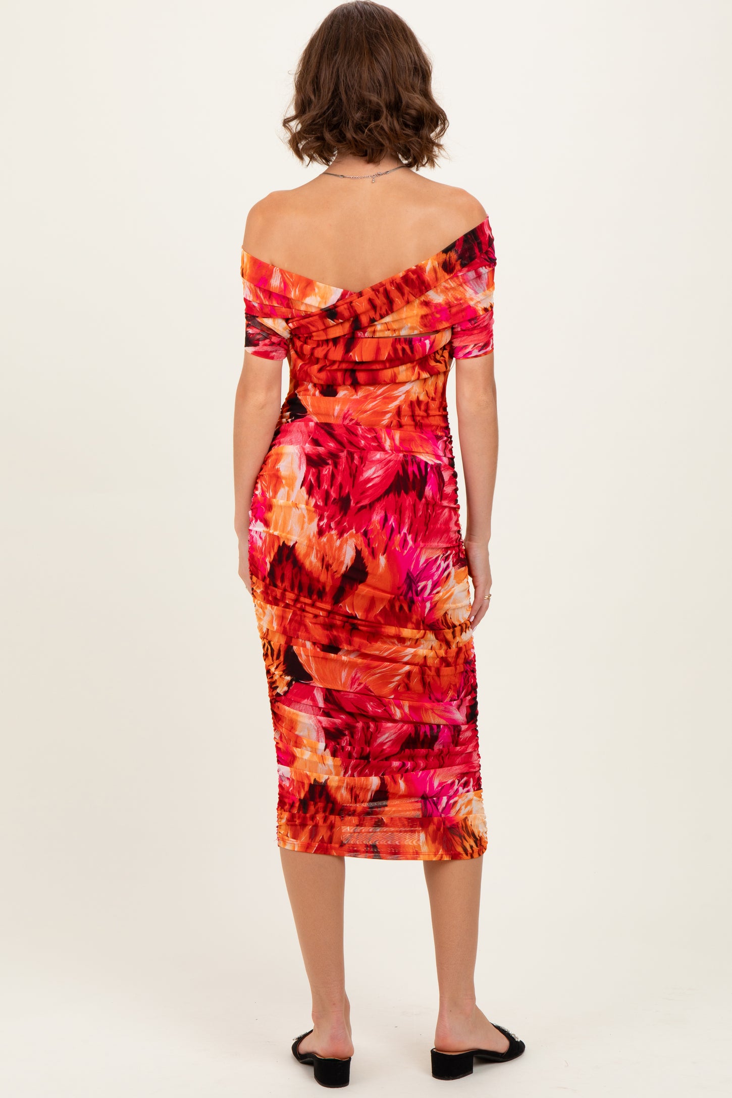 woman wearing a vibrant orange and pink floral off-the-shoulder midi dress, viewed from the back