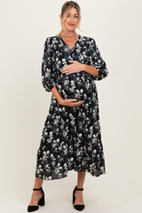 woman wearing a floral black maternity dress with a v-neck and puff sleeves, holding her baby bump