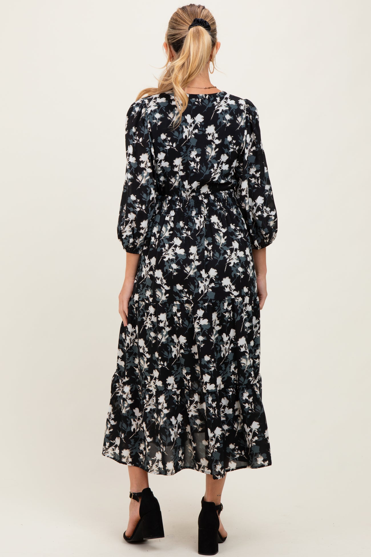 woman wearing a floral black maternity dress with three-quarter sleeves and a tiered skirt, showing her baby bump from the back