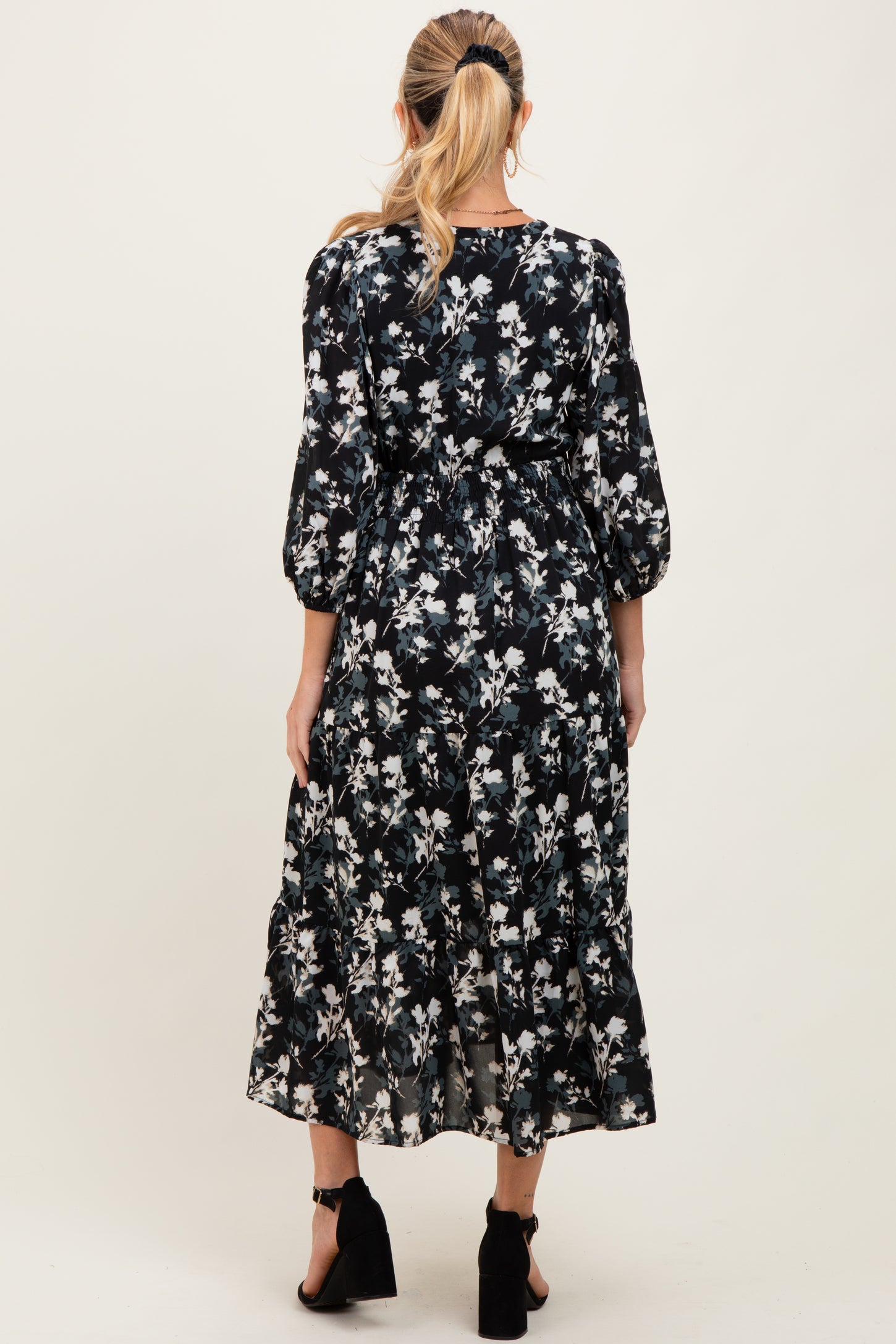 woman wearing a floral black maternity dress with three-quarter sleeves and a tiered skirt, showing her baby bump from the back