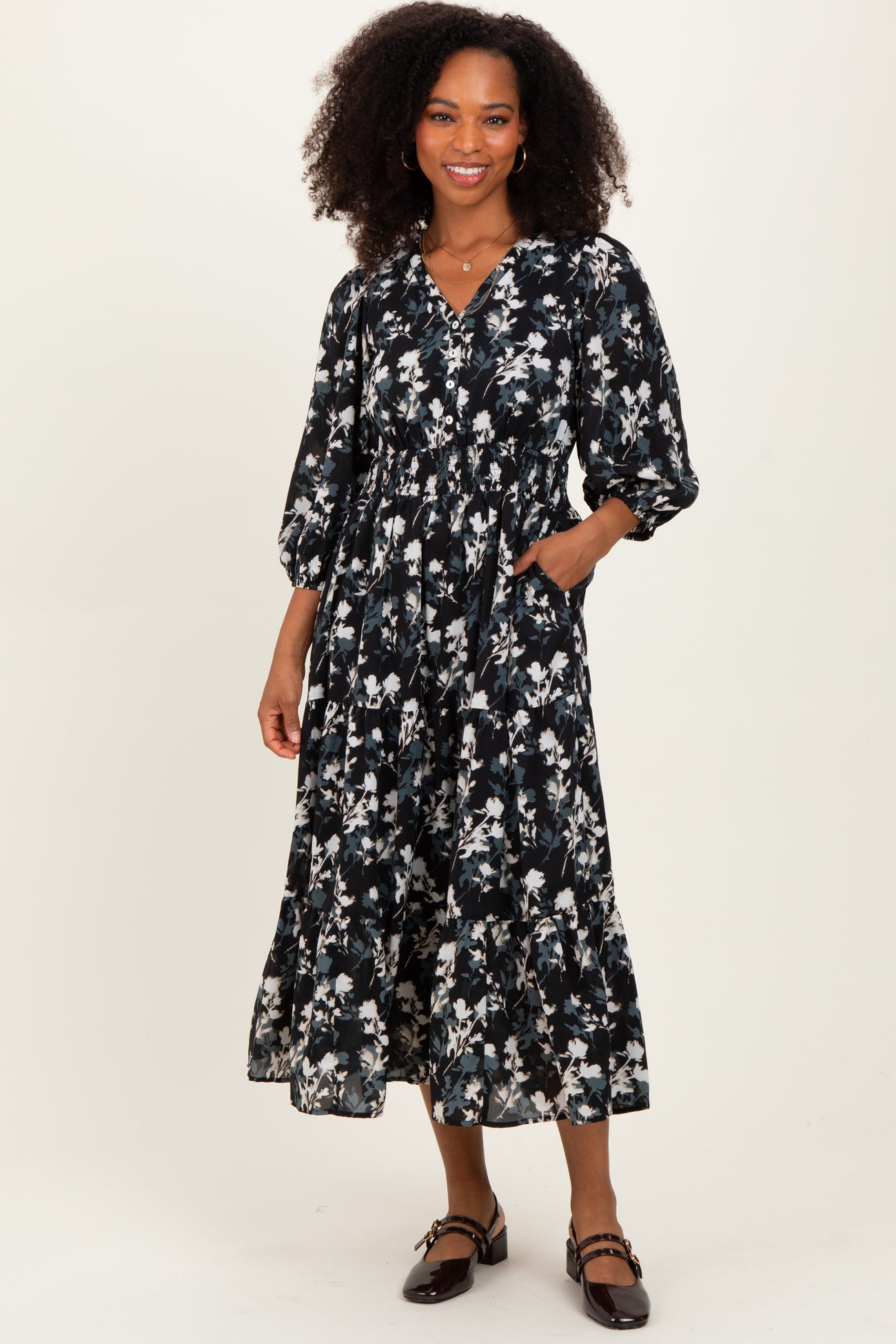 woman wearing a black floral midi dress with puff sleeves and pockets, standing on a neutral background