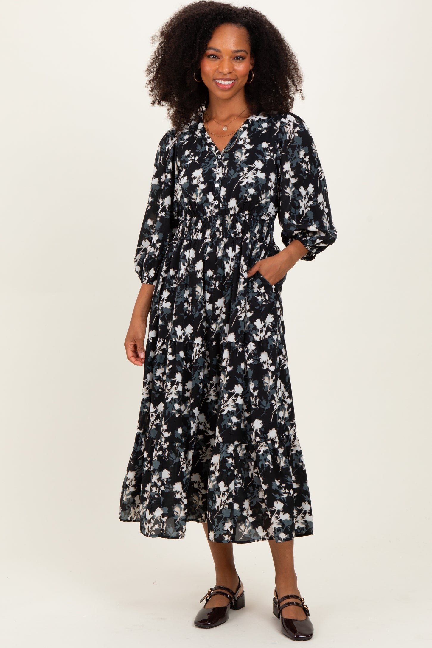 woman wearing a black floral midi dress with puff sleeves and pockets, standing on a neutral background
