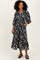 woman wearing a black floral midi dress with puff sleeves and pockets, standing on a neutral background