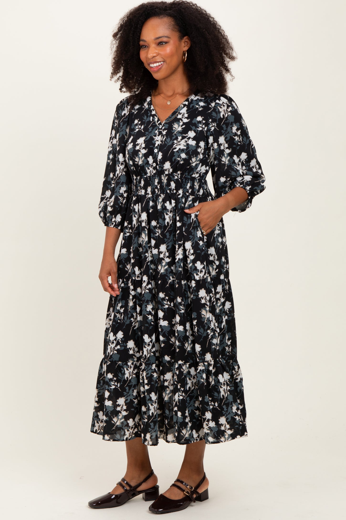 woman wearing a black floral midi dress with three-quarter sleeves and pockets