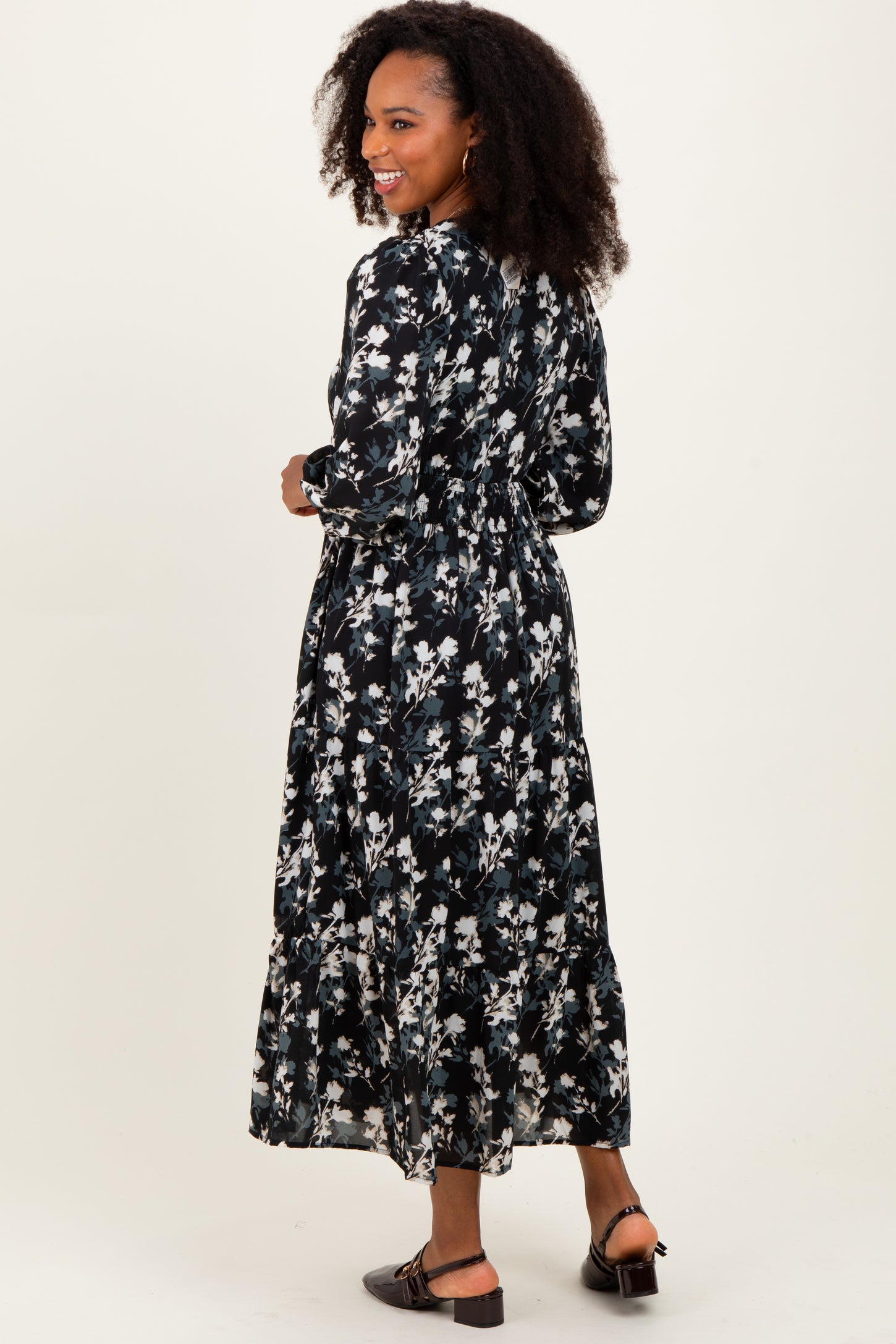 woman wearing a black floral maxi dress with long sleeves and a cinched waist, facing away from the camera