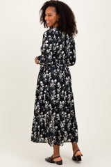 woman wearing a black floral maxi dress with long sleeves and a cinched waist, facing away from the camera
