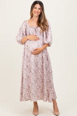 woman wearing a blush floral maternity dress with long puff sleeves and a gathered bodice, holding her baby bump