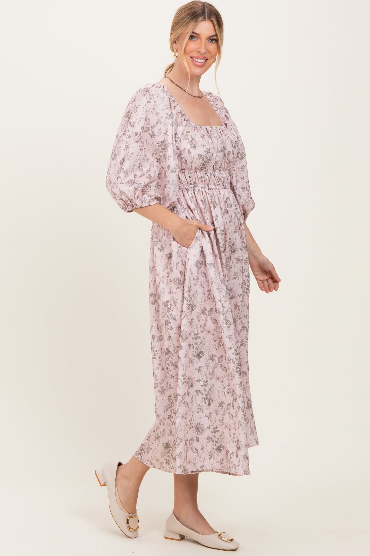 woman wearing a light pink floral midi dress with puff sleeves and pockets