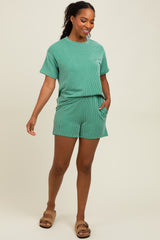 woman wearing a green striped short sleeve top and matching shorts, standing with one hand in her pocket