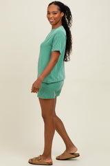 woman wearing a green striped short sleeve top and matching shorts, standing sideways with long curly hair and sandals