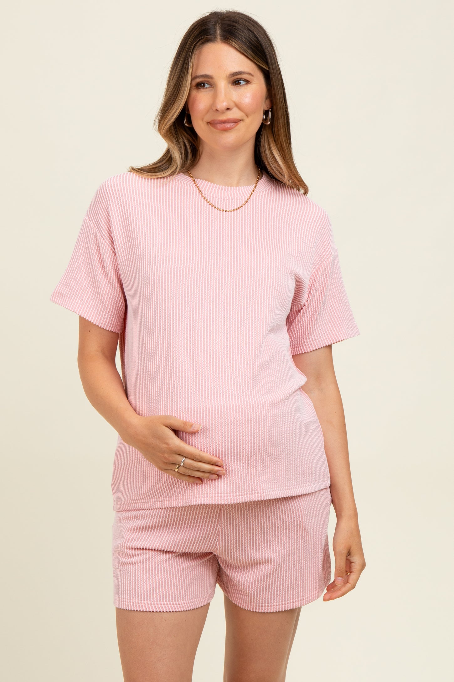 woman wearing a light pink ribbed maternity short set, showing her baby bump and smiling