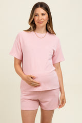 woman wearing a light pink ribbed maternity short set, showing her baby bump and smiling