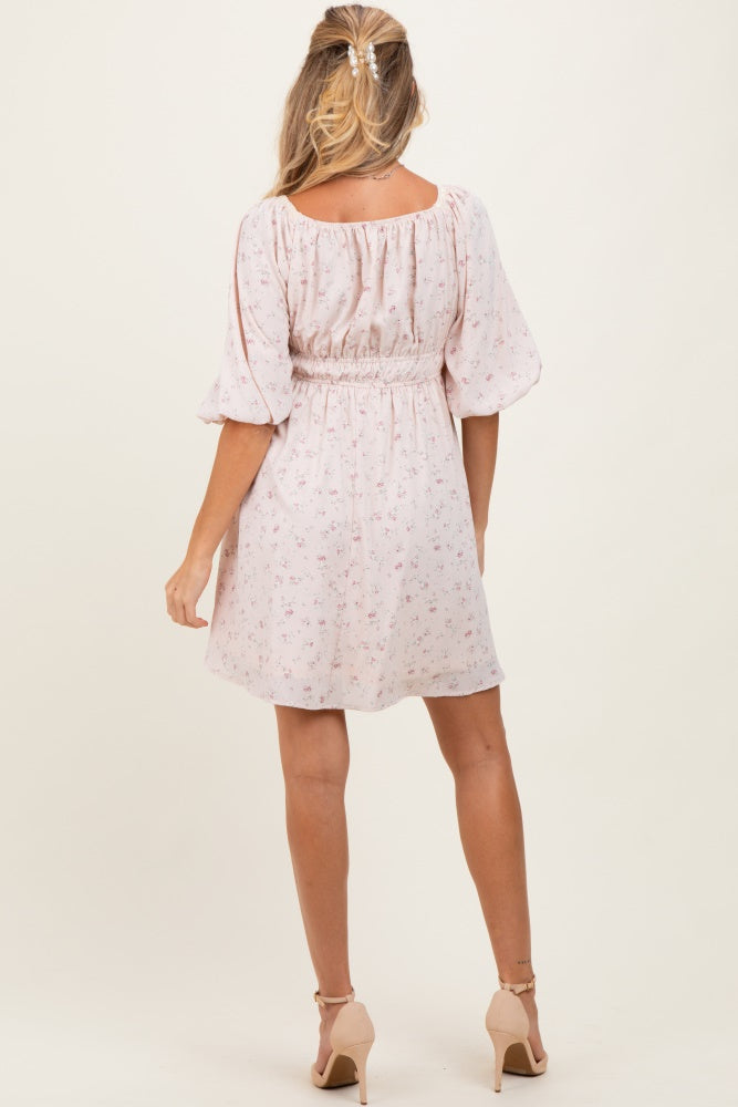 woman wearing a light pink floral maternity dress with a smocked waist and balloon sleeves, shown from the back