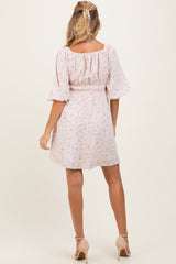 woman wearing a light pink floral maternity dress with a smocked waist and balloon sleeves, shown from the back