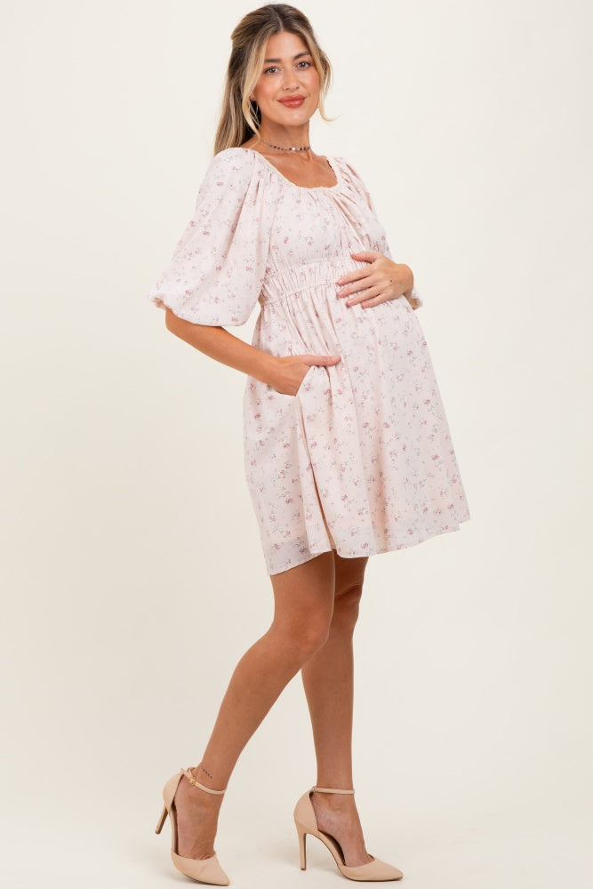 woman wearing a pink floral maternity dress with puff sleeves and pockets, holding her baby bump