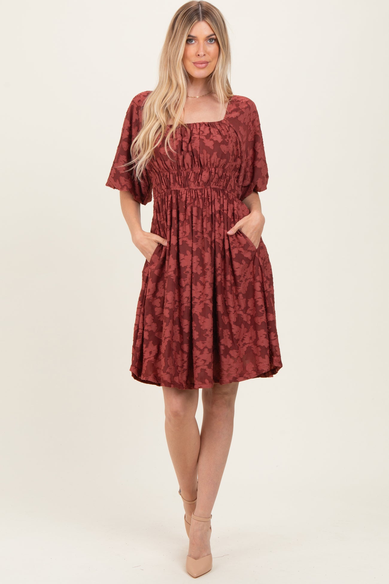woman wearing a rust-colored floral short sleeve dress with a square neckline and pockets