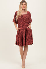 woman wearing a rust-colored floral short sleeve dress with a square neckline and pockets