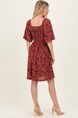 woman wearing a red floral short sleeve dress with a smocked waist and a square neckline, viewed from the back