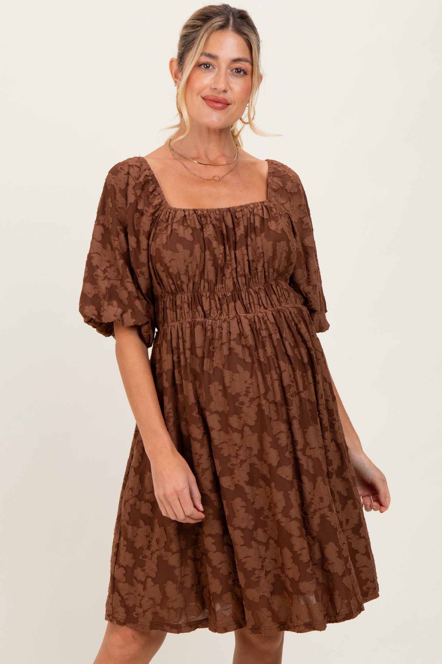 woman wearing a brown maternity dress with a square neckline and puff sleeves, featuring a gathered waistline