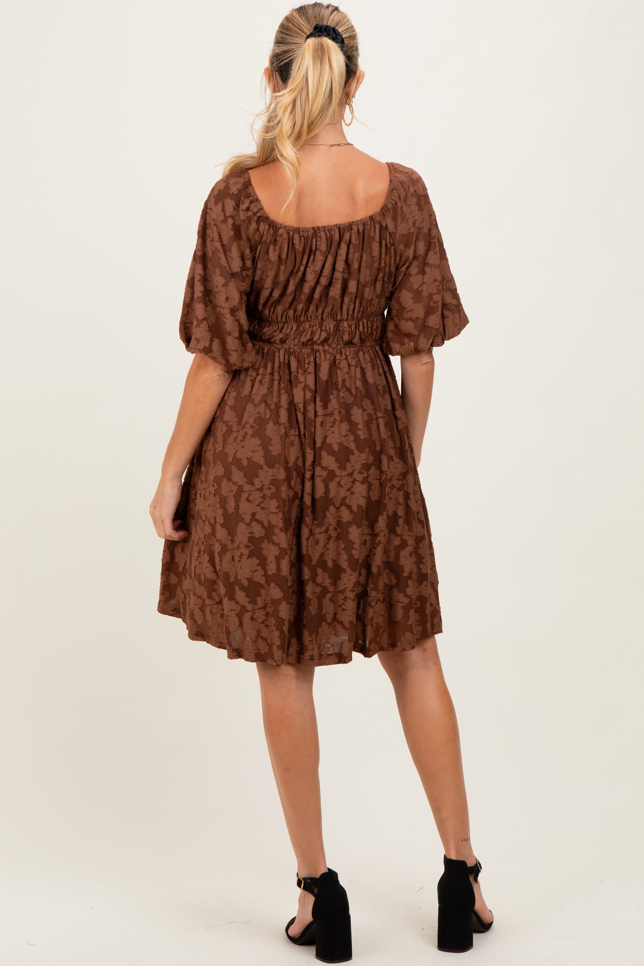 woman wearing a brown patterned maternity dress with puff sleeves and a fitted waist, showing a baby bump from the back