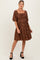 woman wearing a brown floral maternity dress with puff sleeves and a square neckline, standing and smiling