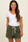 woman wearing a white scoop neck maternity top and green ribbed maternity shorts with a drawstring waistband