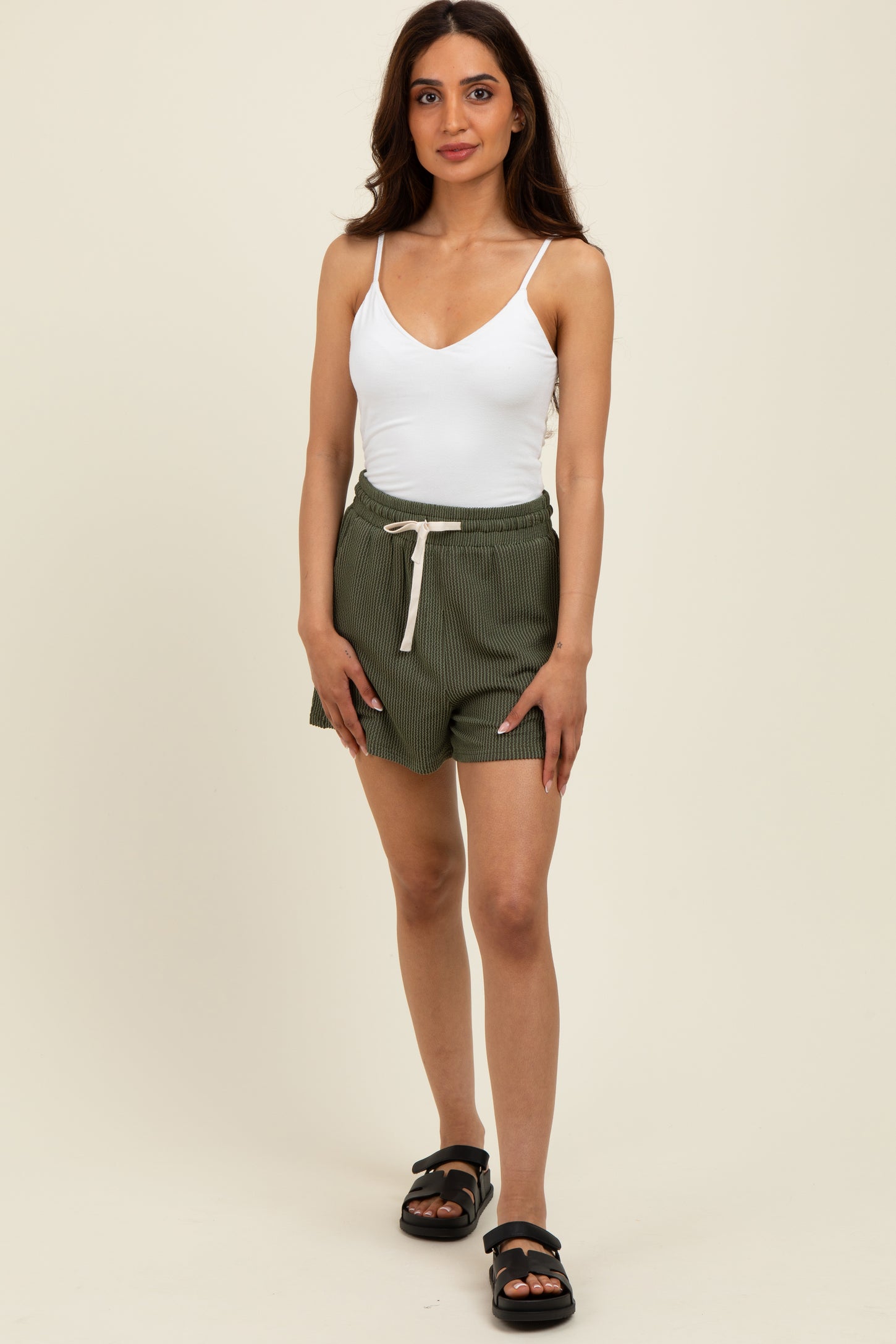 woman wearing a white spaghetti strap tank top and green striped shorts with a drawstring waist