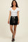 woman wearing a white short sleeve v-neck top and black drawstring shorts, standing and smiling